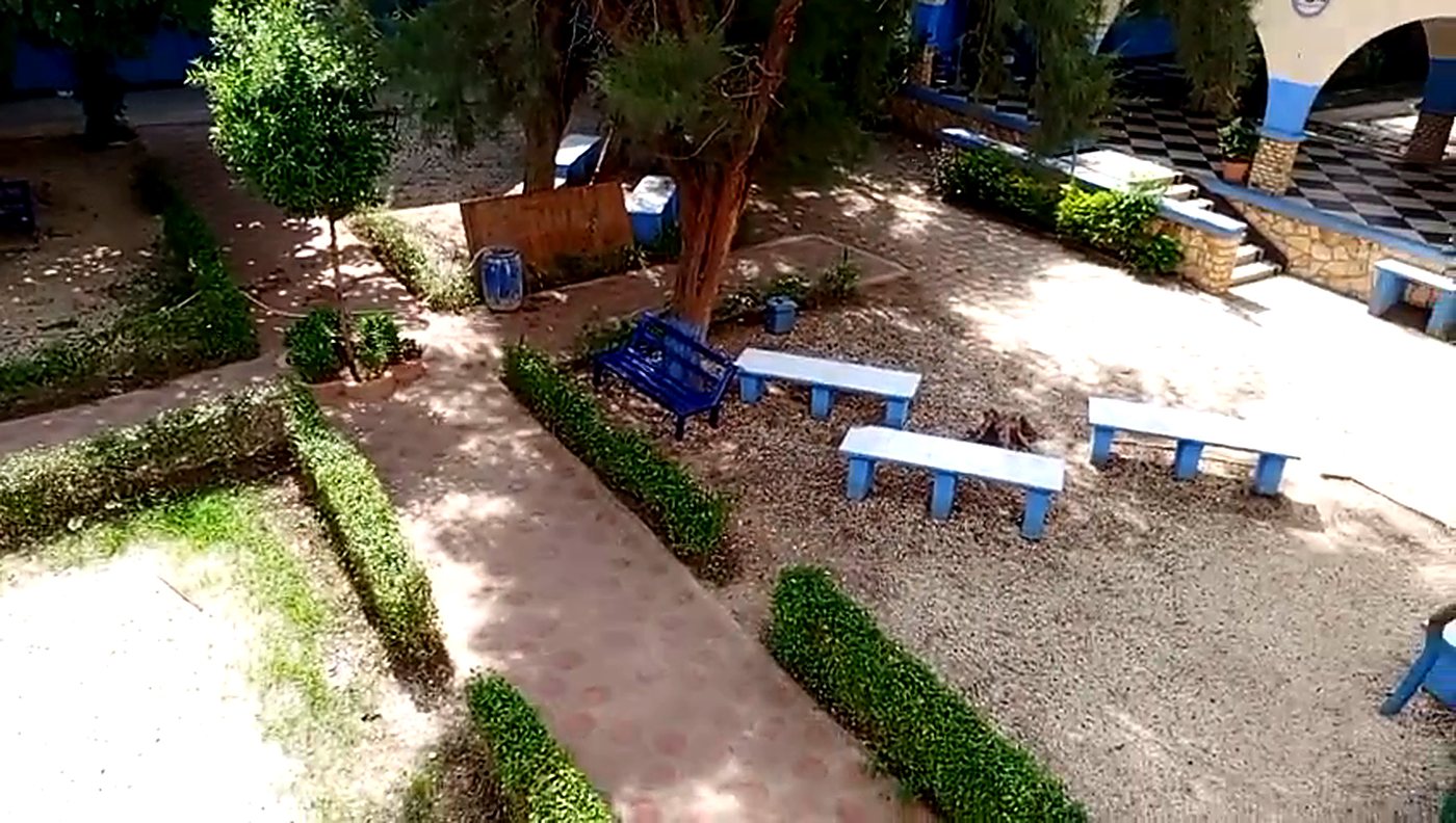 Vue en plongée sur le jardin de l'école, ses haies taillées et ses bancs bleus